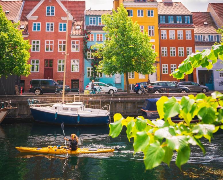 Kvinne i kayakk forbi fargerike kanaler i Christianshavn